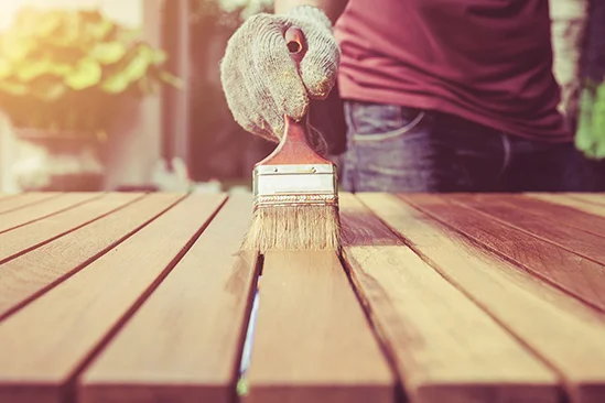 Person streicht Holztisch mit Pinsel.